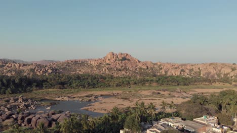 Rocky-landscape-and-barren-Tungabhadra-Riverbank-at-Hampi-town's-edge,-Karnataka,-India---Aerial-Panoramic-shot
