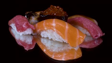Makroansicht,-Die-Nigiri-Sushi-Auswahl-Auf-Schwarzem,-Reflektierendem-Glashintergrund-Dreht,-Toro-Thunfisch,-Lachs,-Zitronenfisch,-Lachsrogen-Und-Grillaal,-Japanische-Küche