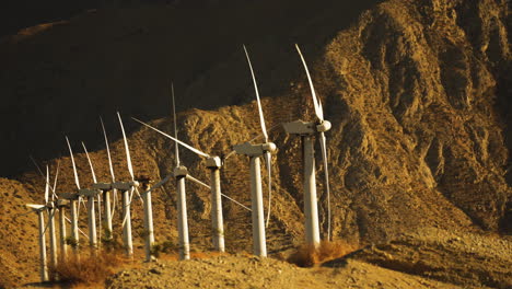 Steady-shiot-of-miniaturised-looking-wind-turbines-rotating-at-a-wind-farm-with-huge-mountain-in-the-background-near-Palm-Springs-in-the-Mojave-Desert,-California,-USA