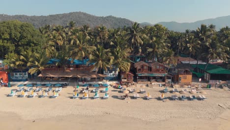 Palolem-Beach-resort-shacks-and-resting-chairs-near-the-coastline-in-exotic-setting---Aerial-Fly-Backwards-Reveal