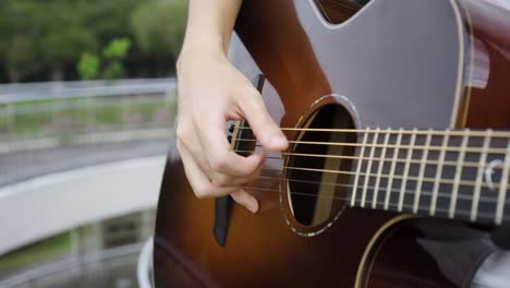 Close-up-shot-of-man-playing-brown-guitar-and-plucking-the-strings-with-scenic-background