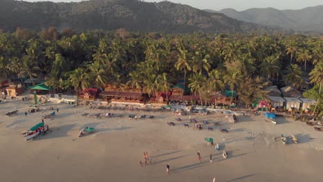Aerial-4k-drone-footage-panning-a-beach-at-sunset-in-Palolem,-India-busy-with-visitors-from-all-over-the-world