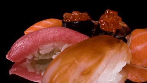 Vista-Macro-Girando-Nigiri-Sushi-En-Vidrio-Negro-Reflectante,-Atún,-Salmón,-Ikura,-Pez-Limón-Y-Unagi,-Comida-Japonesa-Hecha-A-Mano