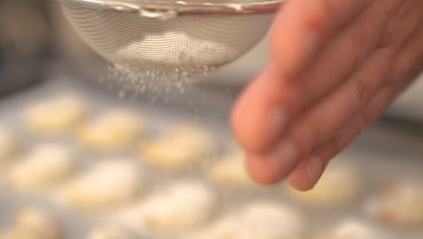 A-baker-sifting-powdered-sugar-on-freshly-baked-Vanilakipferl-cookies