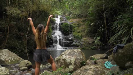 Back-View-Of-A-Brunette-Woman-Raising-Hands-In-The-Air-While-Facing-Stunning-Waterfall---O'Reilly's-Rainforest-Retreat---Gold-Coast,-Australia---medium-shot