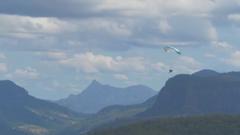 Paragliding-Over-Green-Forest-With-Mountain-Range-In-Background-On-A-Sunny-Day---Gold-Coast-Hinterland,-Australia