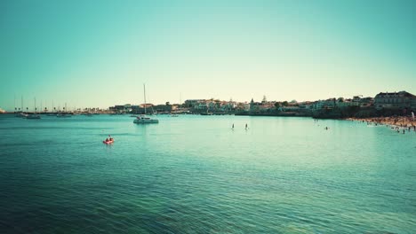 Portugal-Cascais-bay-marina-with-sail-boats,-kayak,-paddle-and-swimming-people-at-sunshine-4K