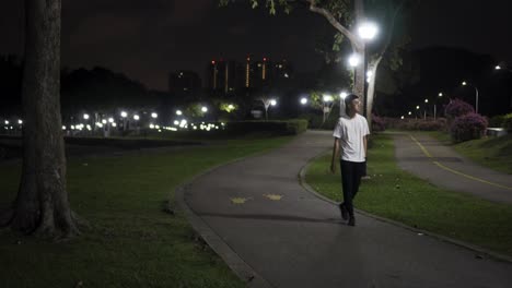 Man-walking-in-the-park-alone-at-night-at-East-Coast-Park,-Singapore-with-bright-street-lights