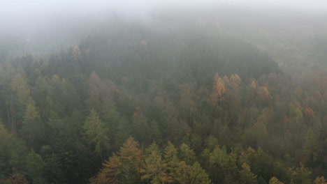 Sideways-aerial-of-autumn-forest-by-clouds-and-fog-in-Central-Europe