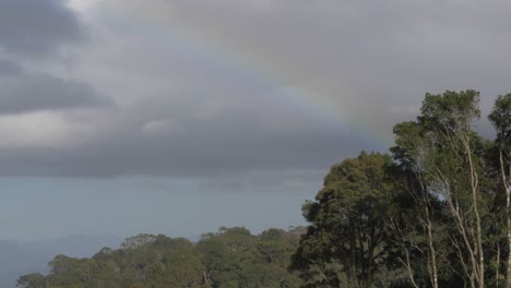 Rainbow-Through-Gray-Clouds-In-Bright-Sky---O'Reilly's-Rainforest-Retreat-In-Lamington-National-Park---Gold-Coast,-Queensland---low-angle-shot