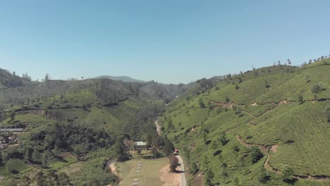 Rural-path-dividing-the-green-lush-hills-and-Tea-plantations-in-Munnar,-India---Aerial-wide-fly-forward