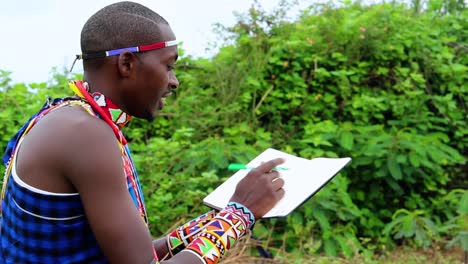 Masai-man-writing-his-thoughts-in-a-notebook,-wearing-tribal-clothing,-in-Africa