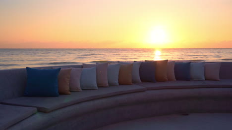Sunset-over-sea-seen-from-beach-lounge-with-pillows-on-seats