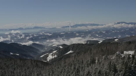 Pohorje-mountains-Slovenia-during-the-winter-with-Kope-Ski-resort-right-and-distant-smoke,-Aerial-flyover-shot