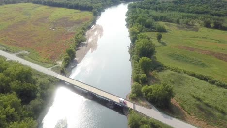 Drone-aerial-view-following-Iowa-River-water-trail-with-highway-bride-at-Hills-Iowa