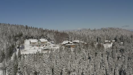 Kope-Ribnica-winter-ski-resort-in-the-Pohorje-mountains-with-bus-and-cars-parked,-Aerial-approach-shot
