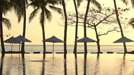 Eine-Goldene-Untergehende-Sonne-Spiegelt-Sich-Im-Wasser-Eines-Luxus-Resort-Swimmingpools-Wider