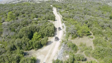 Aerial-follow-shot-of-sandrail-buggy-cars-riding-on-rough-and-unpaved-terrain-amidst-green-land