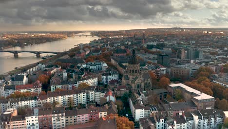 Mainz-City-of-Biontech-showing-the-part-Neustadt-with-the-Christus-Church-and-the-Rhine-river-in-the-back-at-best-orange-fall-light-with-a-aerial-drone-shot