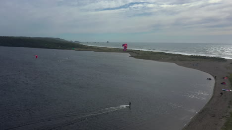 Kitesurfer-Zogen-Mit-Power-Kites-über-Das-Ruhige-Wasser-Des-Floras-Lake,-Wobei-Der-Pazifische-Ozean-Durch-Einen-Schmalen-Strand-Geteilt-Wurde