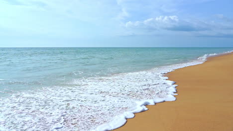 Foam-of-waves-crashing-on-golden-sandy-empty-deserted-beach