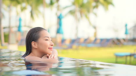 A-pretty-young-woman-leans-her-chin-and-arms-along-the-infinity-edge-of-a-resort-pool
