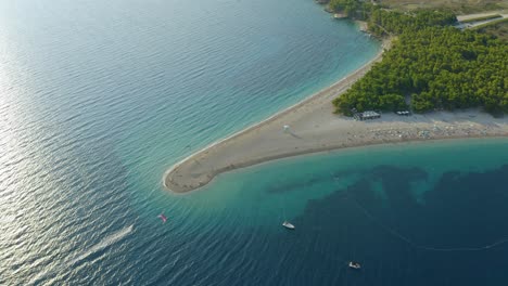 Mesmerizing-aerial-view-of-beach-around-crystal-clear-water-of-sea,-with-tourists-enjoying-paragliding-on-sunny-day
