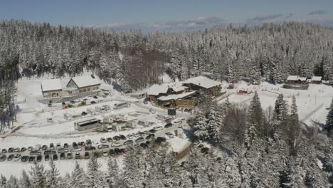 Kope-winter-ski-resort-in-the-snowed-Pohorje-mountains-with-vehicles-parked,-Aerial-approach-shot