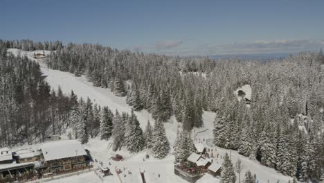 Kope-winter-sports-resort-with-Ribnica-one-track-with-descending-skiers,-Aerial-tilt-down-approach-shot