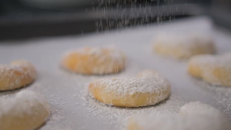 Close-up-of-a-pan-of-freshly-baked-Vanilakipferl-cookies-with-icing-sugar-sprinkling-down-on-them