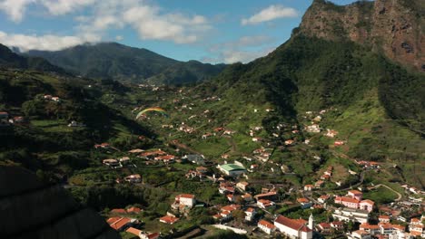 Paraglider-flies-above-small-village-Porto-da-Cruz-on-Madeira-Island,-aerial