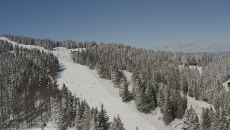 Kope-Slovenia-ski-resort-with-Ribnica-One-track-with-skiers-descending-the-slopes,-Aerial-pan-right-shot