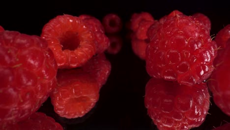 macro-view-passing-through-red-raspberries-on-reflective-black-glass-background,-4k-shot-of-healthy-fresh-fruit,-nutritional-diet