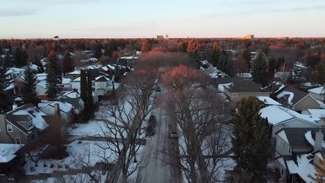 1-4-Aerial-dolly-roll-over-a-luxury-residential-housing-community-at-winter-twilight-sunset-where-the-sun-sets-a-glow-over-the-tall-vintage-tree-tips-over-parked-cars,-empty-sidewalks-and-nobody-out