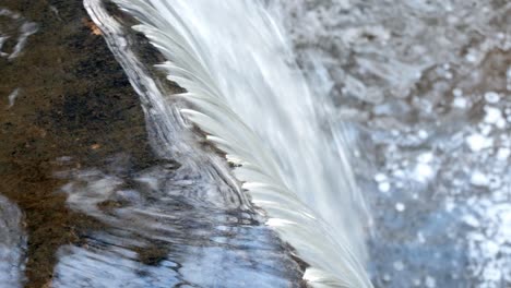Closeup-on-small-splashing-copper-woodland-river-cascading-into-waterfall-dolly-birdseye-right