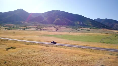 A-drone-follows-a-pickup-truck-on-a-lonesome-road-that-runs-into-a-valley-up-into-the-mountain-range-on-a-clear-summer-day