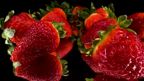 Vista-Macro-Pasando-Por-Fresas-Rojas-Sobre-Fondo-De-Vidrio-Negro-Reflectante,-Toma-Elegante-De-4k-De-Fruta-Fresca-Saludable