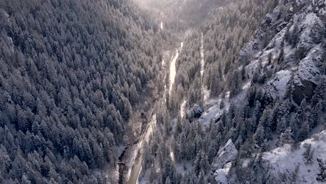 Flying-Over-Country-Road-Between-Forested-Mountain-Slopes-Against-Bright-Sky-During-Winter-At-American-Fork-Canyon,-Wasatch-Mountains,-Utah