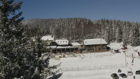 Kope-resort-in-the-Pohorje-mountains-with-people-on-the-snow-playing,-Aerial-dolly-out-reveal-shot