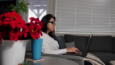 Hispanic-young-female,-working-at-home-on-laptop-during-work-day-hours,-slow-moving-pan-past-plant