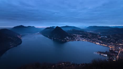 Evening-Timelapse-of-the-city-and-lake-Lugano-from-Monte-Bre,-Switzerland-as-the-city-lights-up
