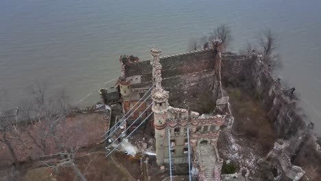 drone-footage-circling-above-the-ruins-of-an-abandoned-castle-on-an-island,-showing-multiple-angles