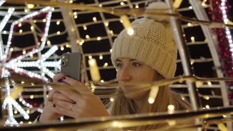 Woman-in-Coat-Photographing-Colorful-Christmas-Decorations-with-a-Phone-at-Night