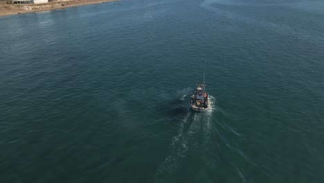 Fishing-boat-motoring-near-the-shoreline,-aerial