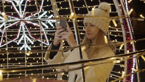 Woman-Photographing-Colorful-Christmas-Decorations-made-of-Lights-with-a-Phone-at-Night