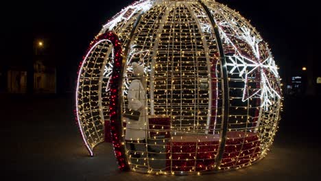 Woman-in-a-White-Jacket-and-Hat-Walking-Inside-A-Giant-Christmas-Tree-Bauble-and-Cheering