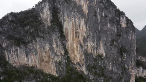 Dramatic-karst-mountain-rock-face,-rugged-texture,-rising-aerial-view