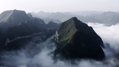 Beautiful-Asian-karst-mountains-rising-above-low-clouds,-aerial-view