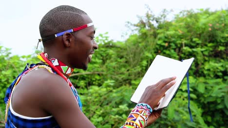 African-man,-smiling,-reading-a-book-outdoors,-wearing-traditional-Masai-clothes