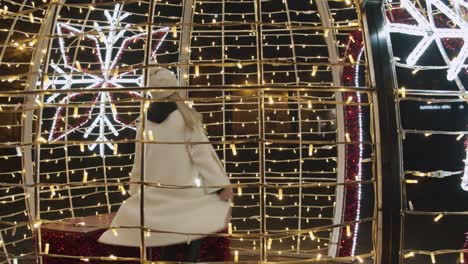 Caucasian-Woman-in-White-Jacket-Dancing-Inside-Christmas-Decoration-of-Lights
